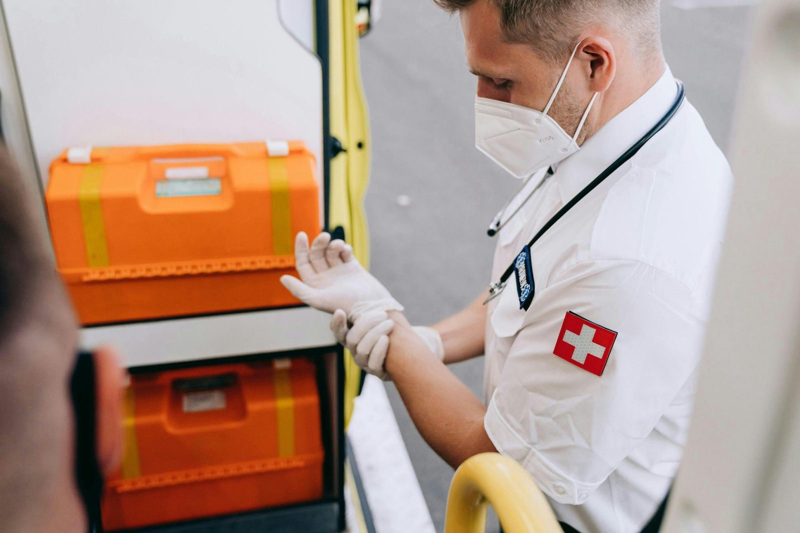 A paramedic putting on gloves next to emergency equipment inside an ambulance.